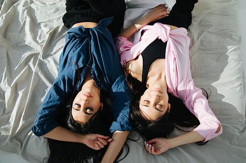 overhead view of two armenian women in casual clothes sleeping on white bedding
