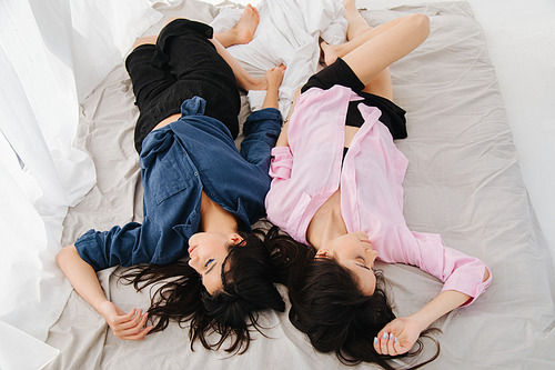 overhead view of two pretty armenian friends sleeping on white bedding