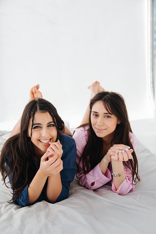young and happy armenian women smiling at camera while lying on white bedding