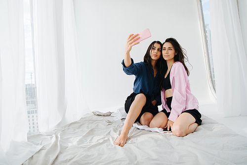young armenian women taking selfie on white bedding at home