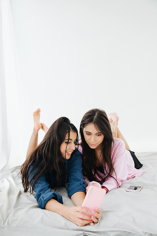 young, pretty armenian friends looking at smartphone while lying in bedroom