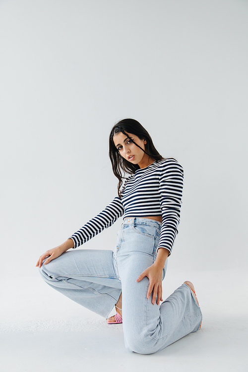 pretty armenian woman in jeans and striped pullover posing on white background