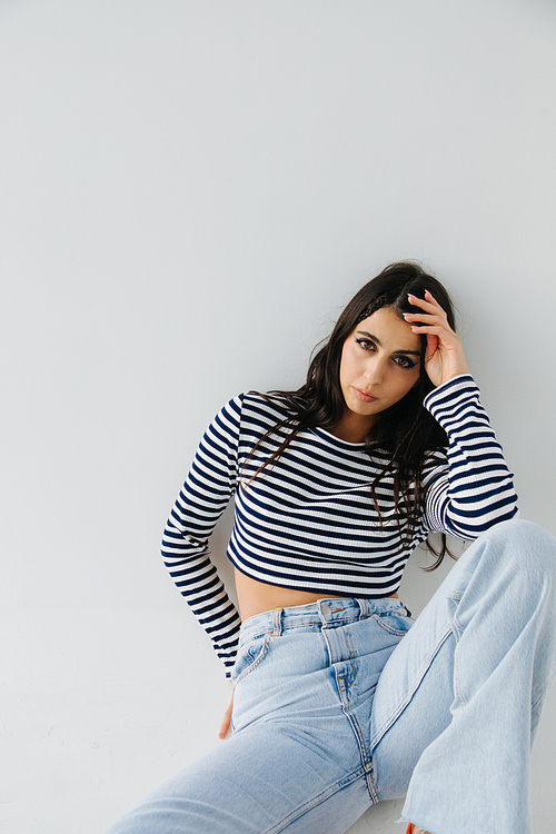 brunette armenian woman in striped pullover and jeans sitting on white