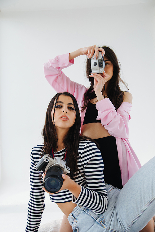young and stylish armenian women with digital cameras on white background
