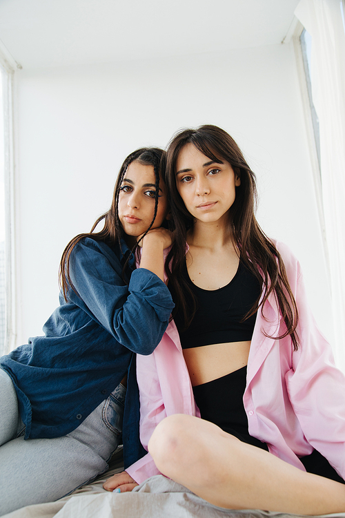 young armenian woman leaning on shoulder of friend while sitting on bedding
