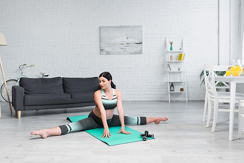 pregnant woman stretching in splits pose on yoga mat in living room
