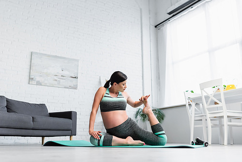 pregnant woman stretching in seated pose on yoga mat at home