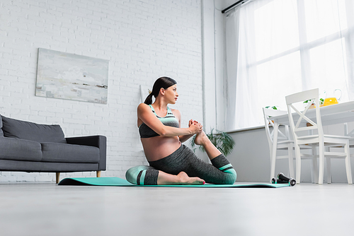 surface level view of young pregnant woman stretching in yoga pose at home