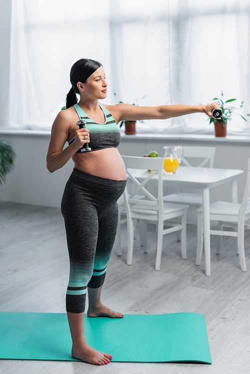 barefoot pregnant woman training with dumbbells while standing on fitness mat