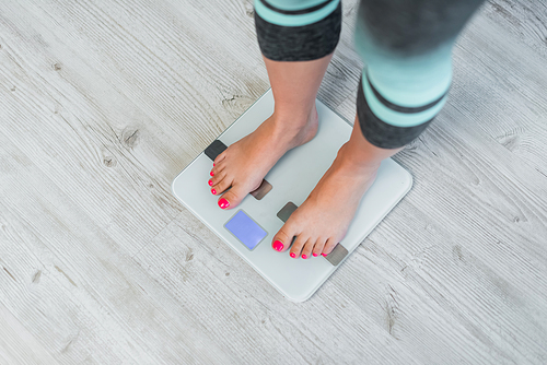 partial view of barefoot woman measuring body weight on floor scales