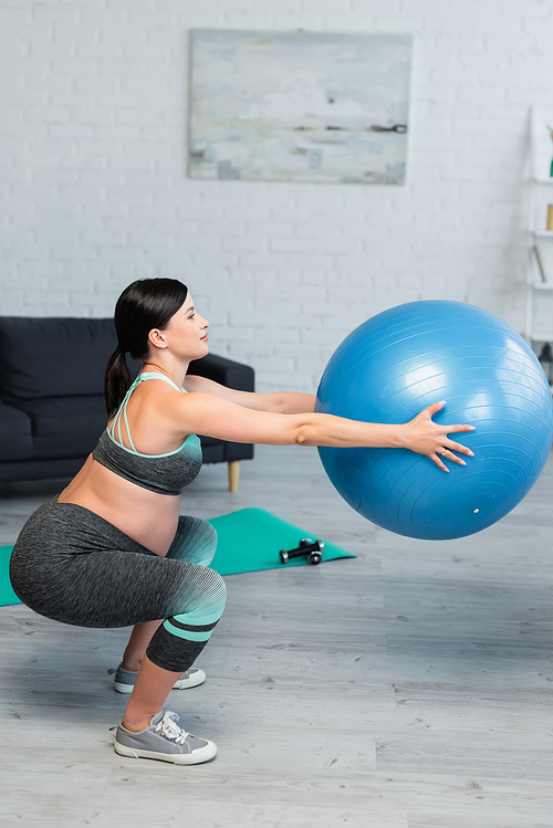 side view of pregnant woman doing sit ups with fitness ball at home