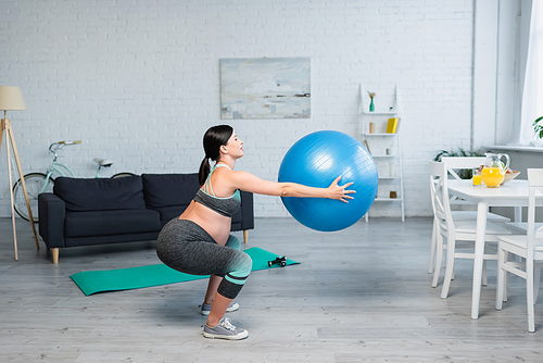 side view of pregnant woman doing sit ups with fitness ball near table with fresh orange juice