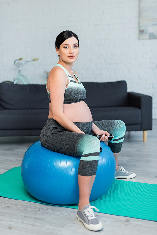 pregnant woman with dumbbells  while training on fitness ball