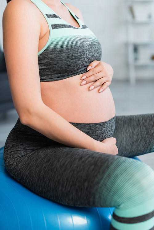 cropped view of pregnant woman in sportswear touching belly while exercising on fitness ball