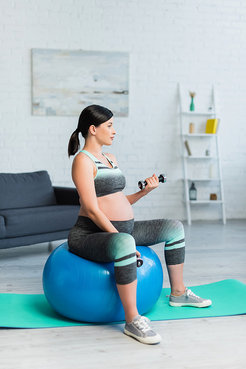 young pregnant woman working out with dumbbells on fitness ball in living room