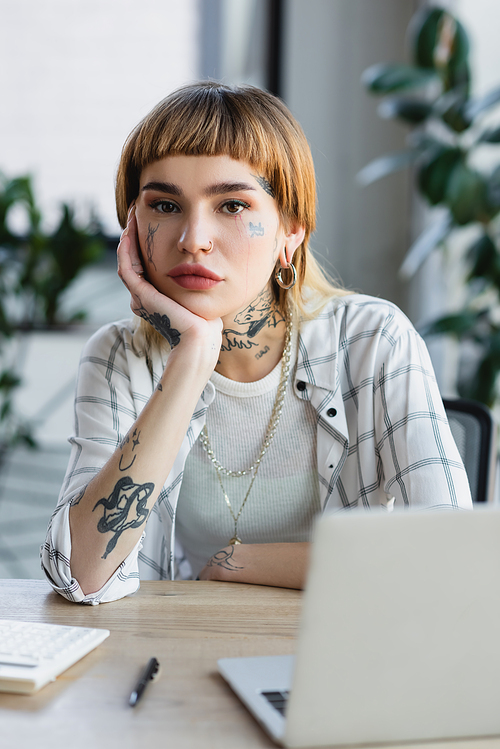 young woman with tattoo and piercing  while sitting near blurred laptop