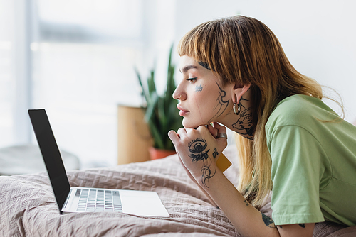 side view of tattooed woman with credit card looking at laptop while lying on bed