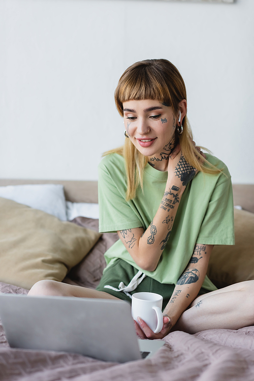 positive woman with tattooed body watching film on laptop in bedroom