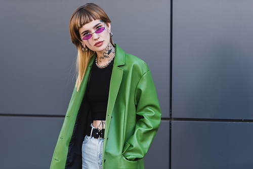 tattooed woman with piercing  while posing with hand in pocket of green jacket