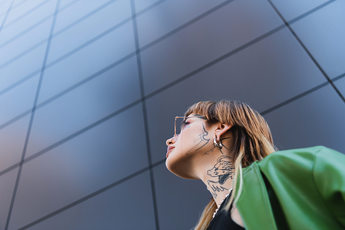 low angle view of stylish tattooed woman near high grey wall on urban street
