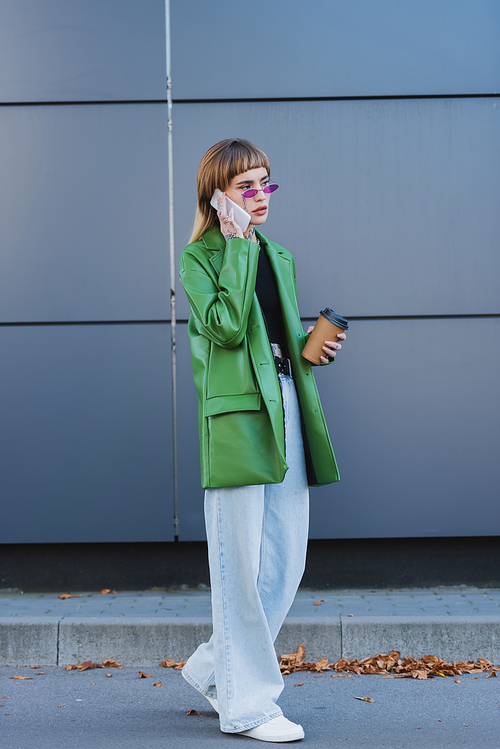 full length view of stylish woman with takeaway drink talking on smartphone outdoors