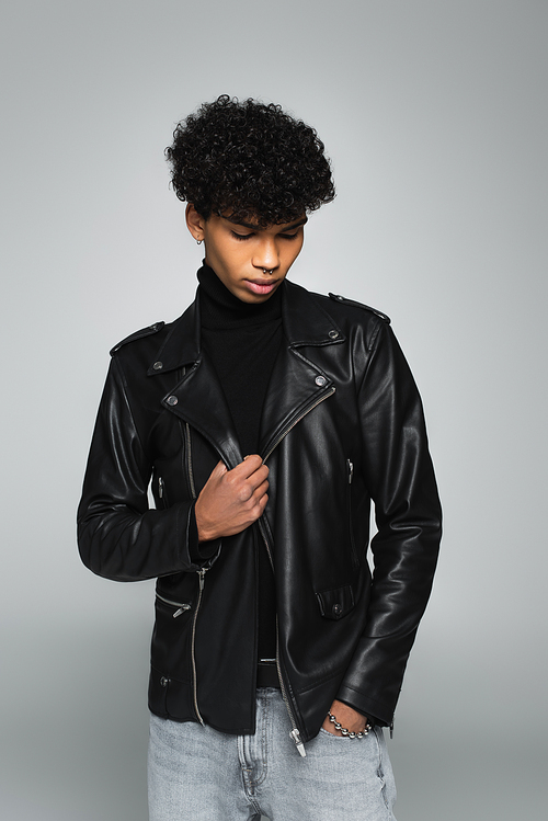 young african american man in black leather jacket posing with hand in pocket isolated on grey