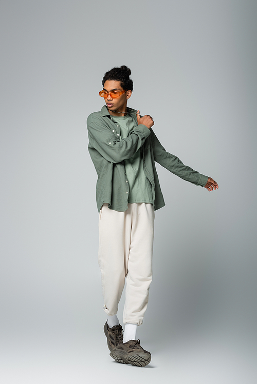 full length view of african american man in shirt and white pants posing on grey background