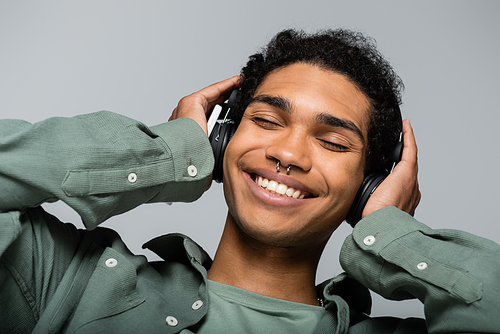 happy african american guy in headphones listening music with closed eyes isolated on grey