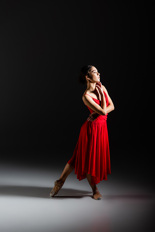 Side view of classical dancer in pointe shoes standing on black background