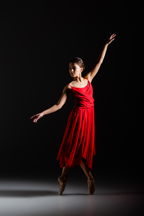 Ballerina in red dress dancing on black background