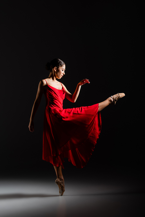 Side view of ballerina dancing on black background