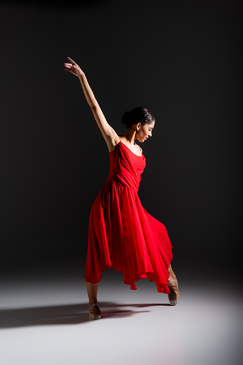 Side view of young ballerina dancing on black background