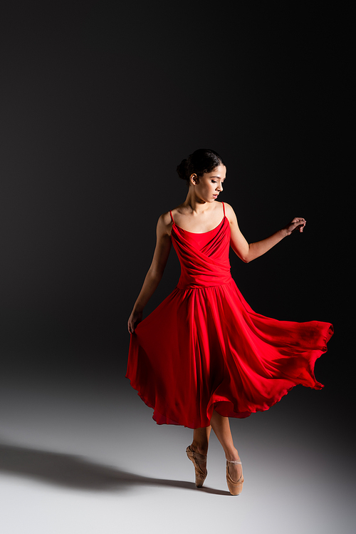 Young brunette ballerina in red dress dancing on black background