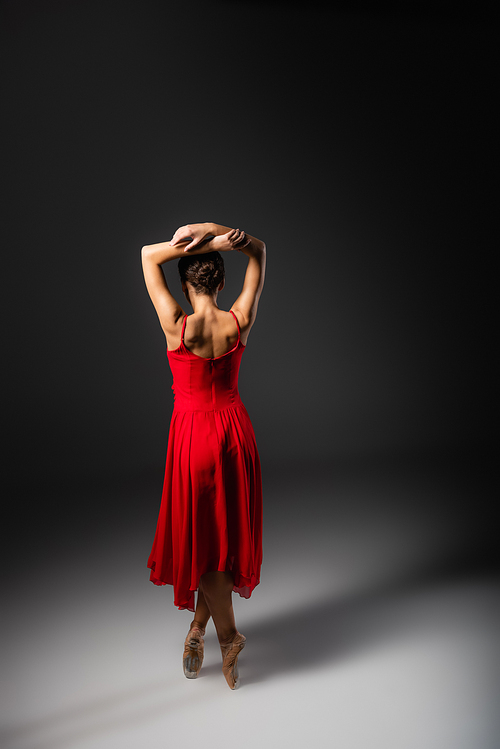 Back view of ballerina in red dress and pointe shoes standing on black background