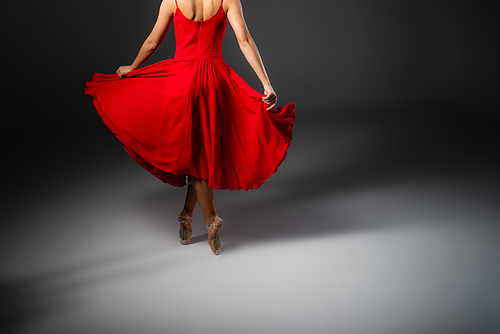 Cropped view of ballerina in red dress dancing on black background