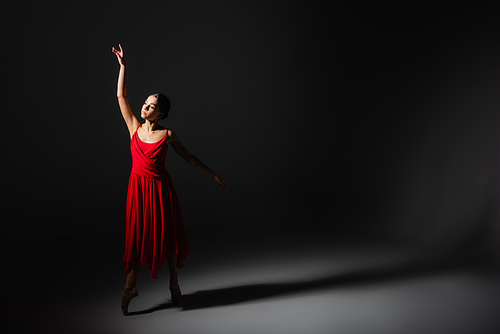 Ballerina in red dress dancing in light on black background
