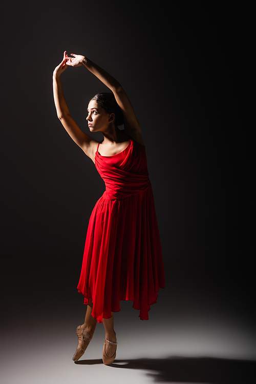 Side view of woman in pointe shoes dancing on black background with light