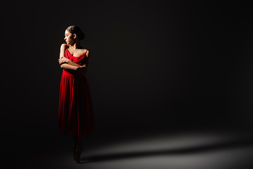 Side view of ballerina in red dress dancing in light on black background