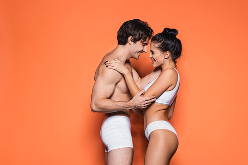 side view of happy and sexy couple in white underwear standing on orange