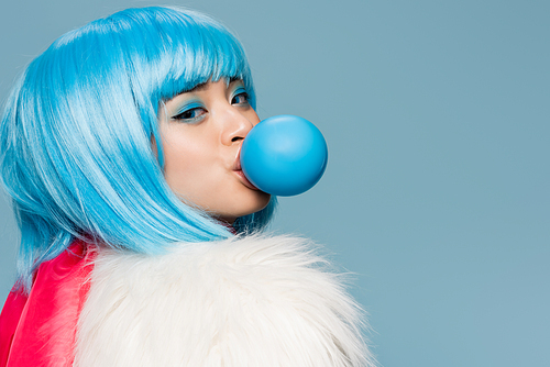 Pretty asian woman in furry jacket blowing bubble gum and  isolated on blue