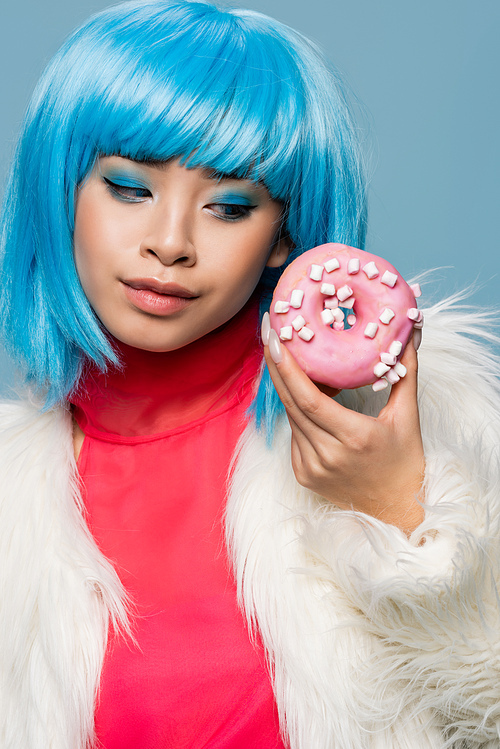 Portrait of stylish asian woman looking at donut with glaze isolated on blue