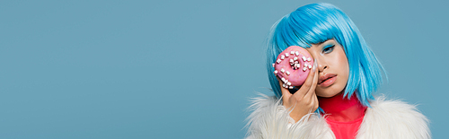 Stylish asian woman holding donut with glaze near face isolated on blue, banner