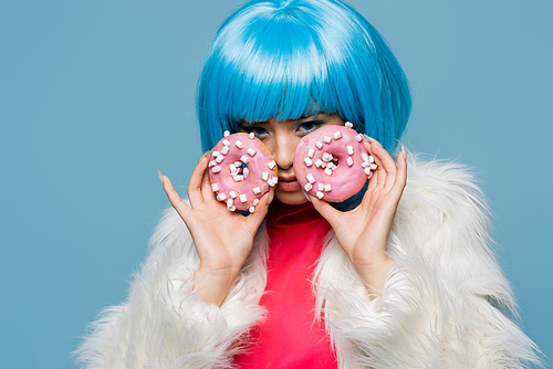 Asian pop art woman holding tasty donuts near face isolated on blue