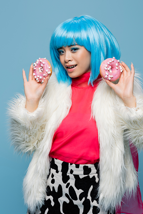 Cheerful asian woman in pop art style holding donuts with glaze isolated on blue