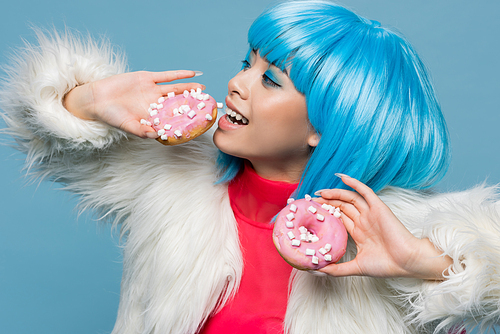 Positive asian pop art woman holding delicious donuts isolated on blue