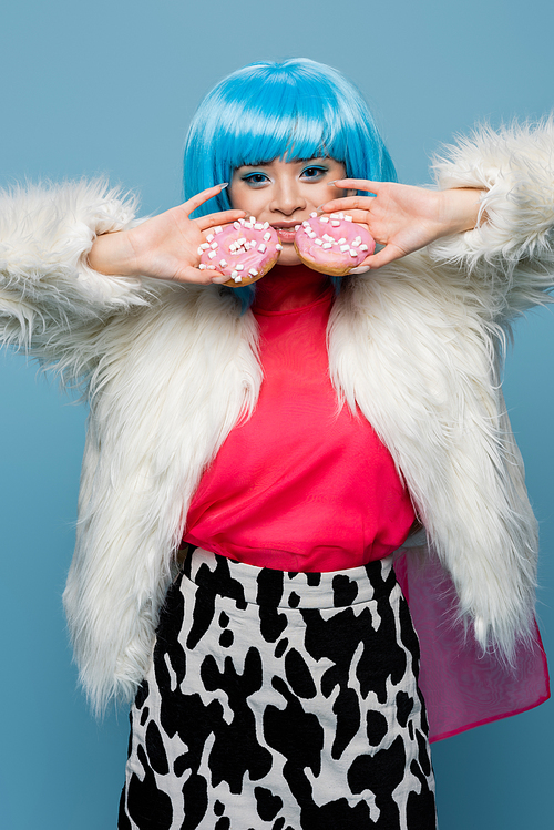 Smiling asian woman in pop art style holding donuts isolated on blue