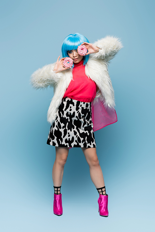 Full length of stylish asian woman posing with donuts on blue background