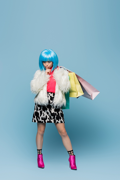 Asian woman in pop art style holding shopping bags and showing secret gesture on blue background