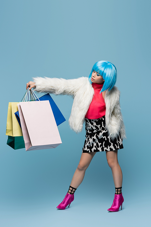 Pretty asian woman in pop art style looking at shopping bags on blue background