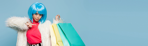 Stylish asian pop art woman pointing at colorful shopping bags isolated on blue, banner